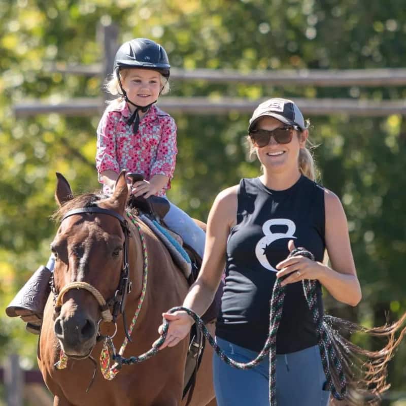 Young girl on horseback in Western riding lesson, being led by Jen Byvelds.